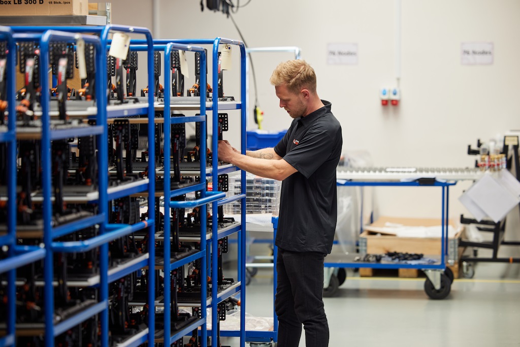 Kevin Magnussen i produktionen, sammen med nogle af Asetek SimSports første pedalsæt, der bliver håndsamlet.